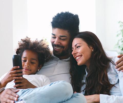 Three person family smiling and sitting on a couch together