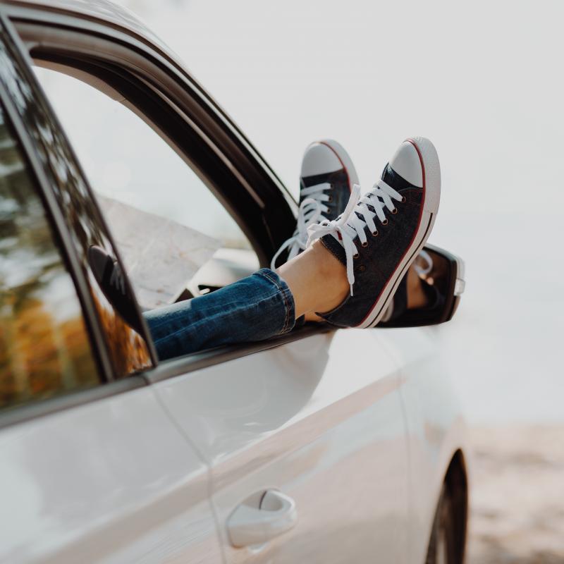 Relaxed posture, legs out car door window. Car parked overlooking beach.